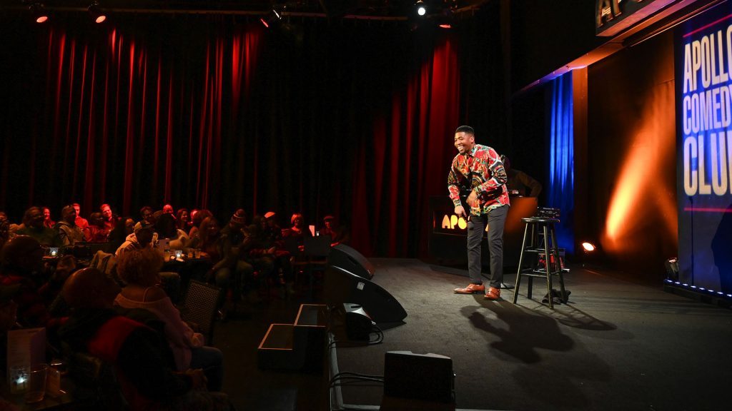 A man standing on stage performing at Apollo Comedy Club
