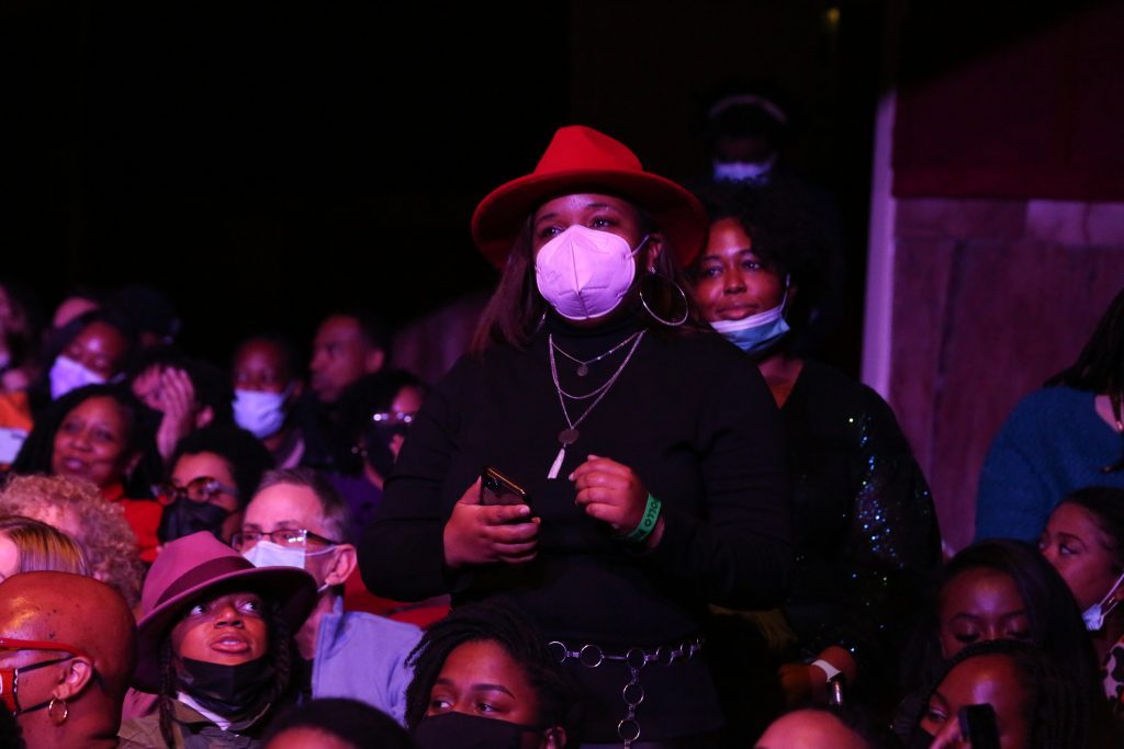 A woman in a mask standing in the crowd during a performance