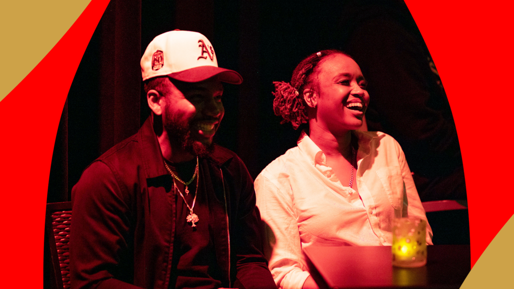 A man and a woman sitting together, laughing at Apollo Comedy Club.